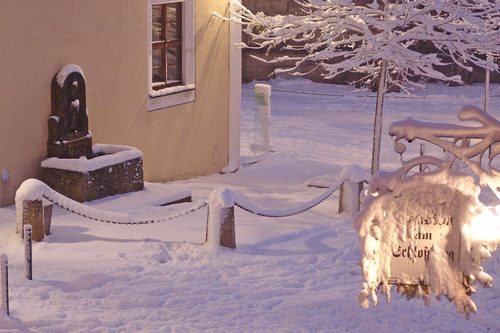Verschneiter Innenhof bei Nacht mit beleuchtetem Pensionsschild