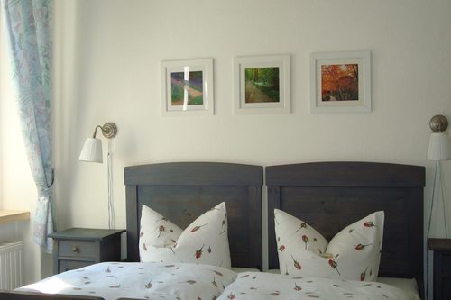 Doppelzimmer mit zwei Betten und gerahmten Bildern über dem Kopfteil
